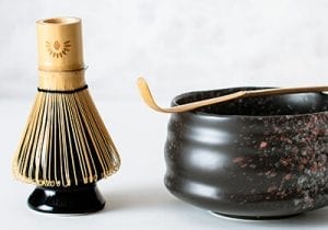 Chasen Matca Whisk On a Ceramic Holder Next To A Ceramic Chawan Matcha Bowl With A Chashuku Bamboo Spoon On Top